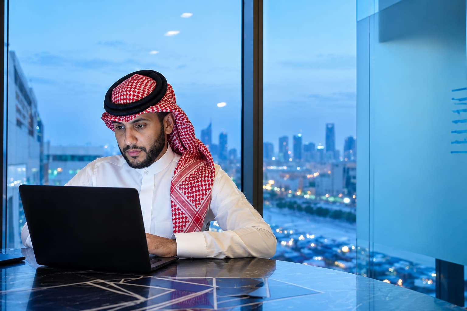 موظف يعمل على حاسوبه في مكتب يطل على الرياض مساءً